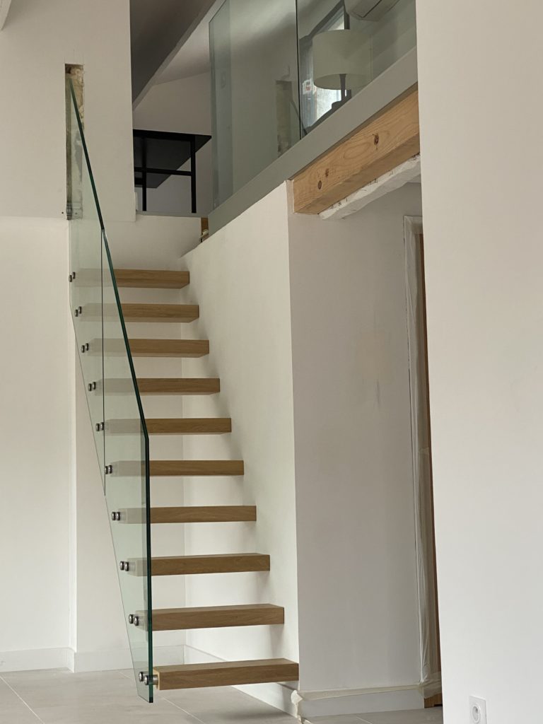 Escalier design suspendu avec marches en bois clair et garde-corps en verre